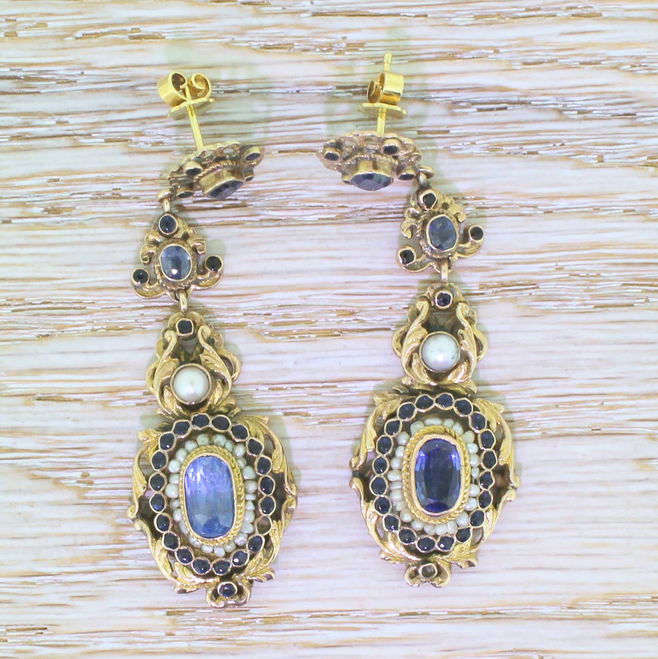 A bold and decorative pair of Austro Hungarian earrings, featuring an estimated total of 6.50 carat of natural, unenhanced blue sapphire and natural seed and one undrilled button pearl. A thrilling and high end example of the neo-renaissance /