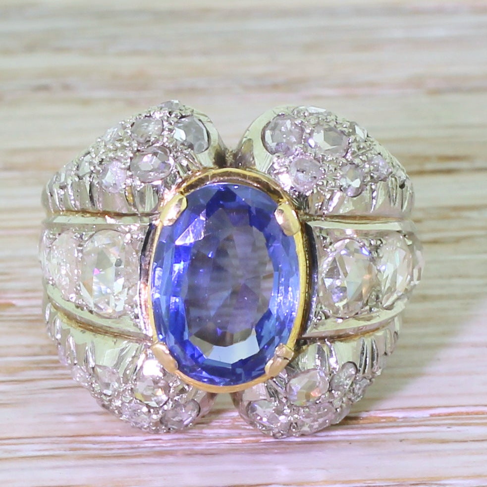 Oval mixed cut sapphire and rose cut diamonds rest in the shoulders of this ring, and they graduate in size as the ring widens. Crowning the piece is a fine natural and unheated sapphire which is so blue you’d swear it was lit from within. The two