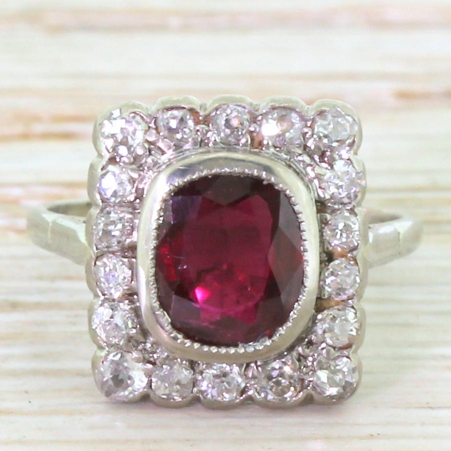 A fabulous cluster ring featuring a cushion shaped ruby in milgrained rubover setting. Surrounded by 18 old cut diamonds in a square cluster leading to a fine platinum band. A unique, characterful and striking Art Deco beauty.

Accompanied by an