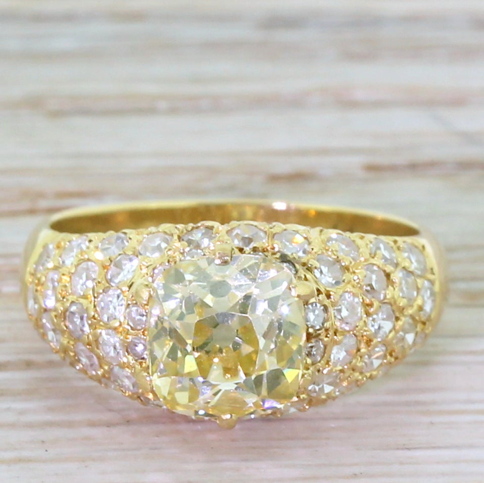 This certainly makes a statement! Centred by a vibrant cushion shaped old mine cut diamond of a fancy light greenish yellow, the colour of which is emphasised by the 51 high-white pavé-set eight cuts in the surround. This glitter ball of a ring is