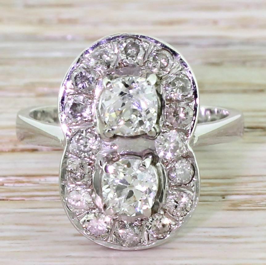 Gloriously bold. The two feature old cut diamonds are wonderfully bright and vibrant, and are claw set within a surround of sixteen eight-cut diamonds. The quite lovely scrolling open gallery leads to a chunky tapering band. An assertively beautiful