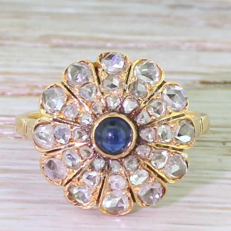 Desperately pretty and unique. A small deep blue cabochon sapphire sits in the centre of this beautifully realised cluster ring. With twelve graduating “rays” emanating from the centre, each set with three rose cut diamonds. The ornate hand-carved