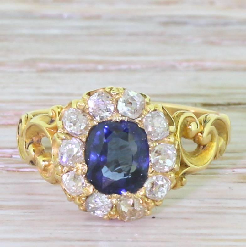Exceptional in every way. The rich, blue cushion cut sapphire is surrounded by ten high white old mine cut diamonds. Set nice and low to the finger on a simple gallery which leads to a gloriously ornate asymmetrical band.

The engraving to the