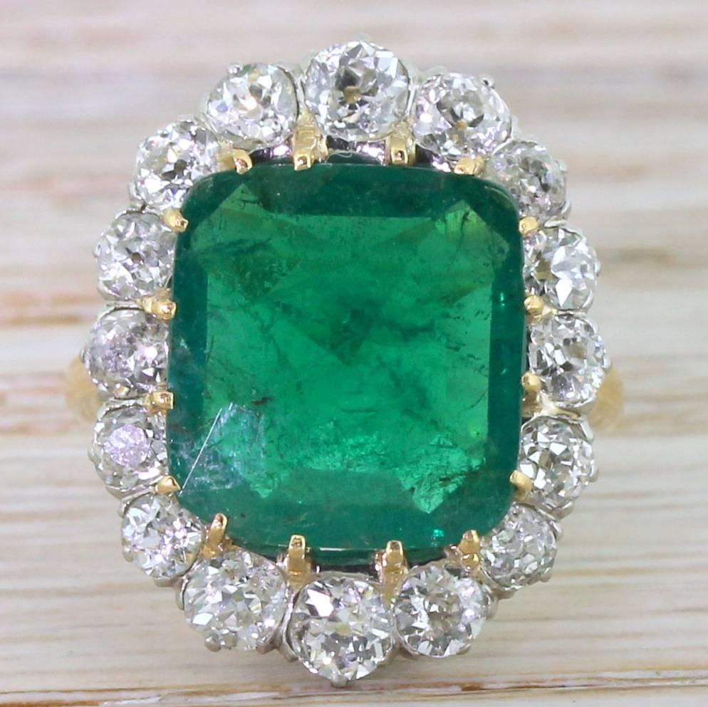 A magnificent, magnificent Colombian emerald. The central stone – a deep, rich and glowing green – is claw set within a surround of sixteen old cut diamonds of graduating size set in a finely pierced platinum gallery. A high class, high spec ring