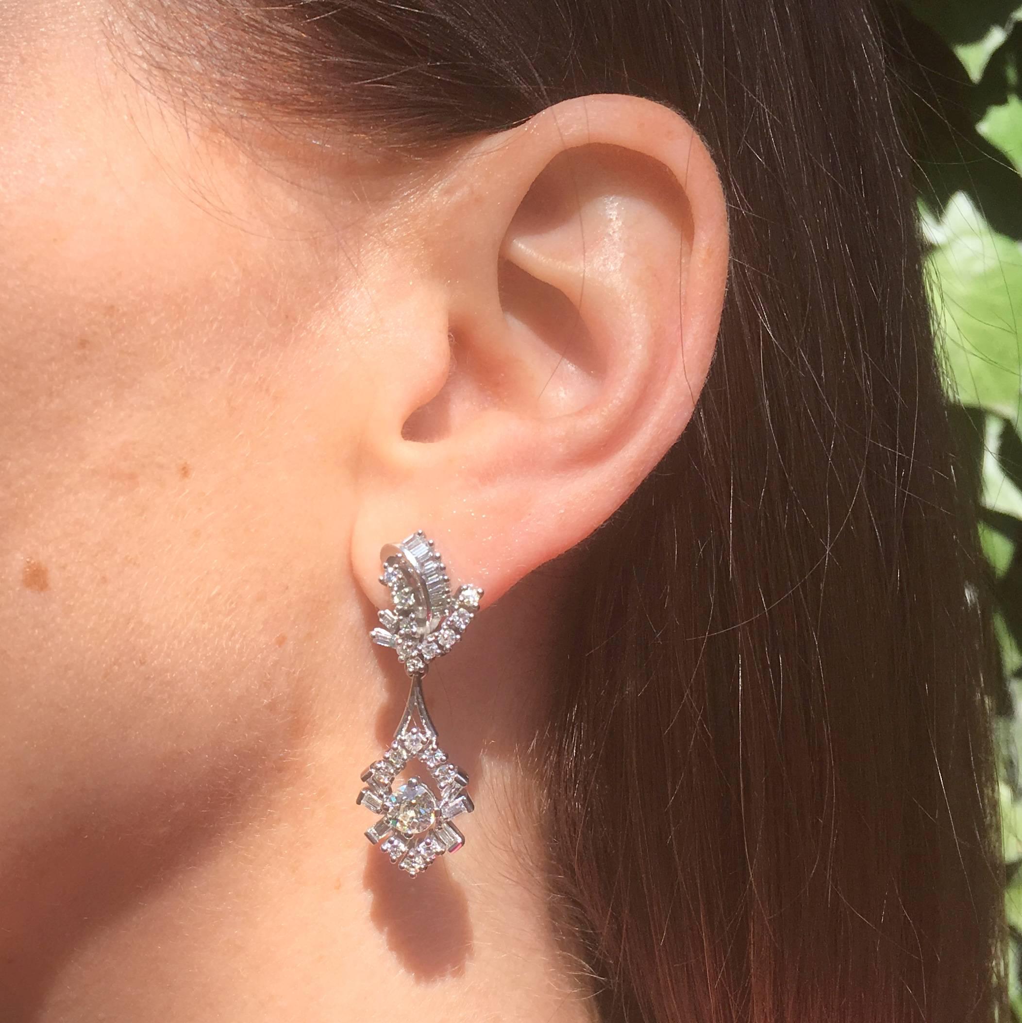 Stunningly realised diamond drop earrings. The asymmetrical top part of the earrings is set with a sweeping line of eight baguette cut diamonds set within a 