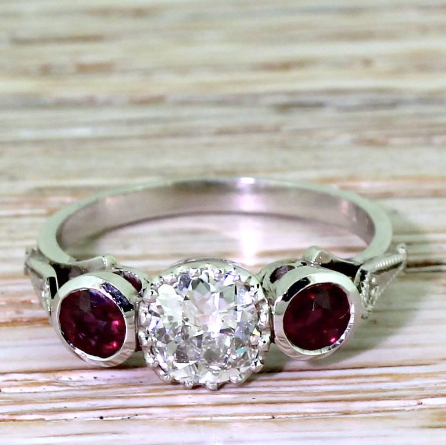 High class and unique. The centre bright and lively old cut diamond - approximately 0.75 carat - is in an ultra fine sixteen claw collet. A pair of natural, unheated rubies flank the main stone in rubover collets. Spear-shaped milgrain shoulders