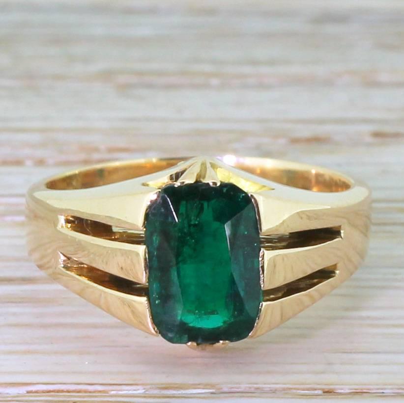 A glowing cushion shaped blue-green emerald contrasts beautifully with the red gold mount. The stone is securely claw set with tri-vented shoulders leading to a nicely weighty shank. A striking ring that would work equally well as a dress ring or an