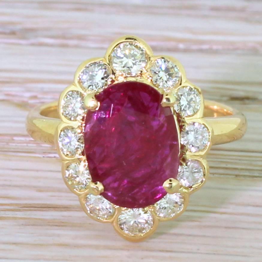 A striking and beautiful cluster ring. The glowing and almost impossibly bright ruby is framed by twelve high white brilliant cut diamonds. The diamonds at the top and the bottom of the cluster are slightly larger than the other then, giving the