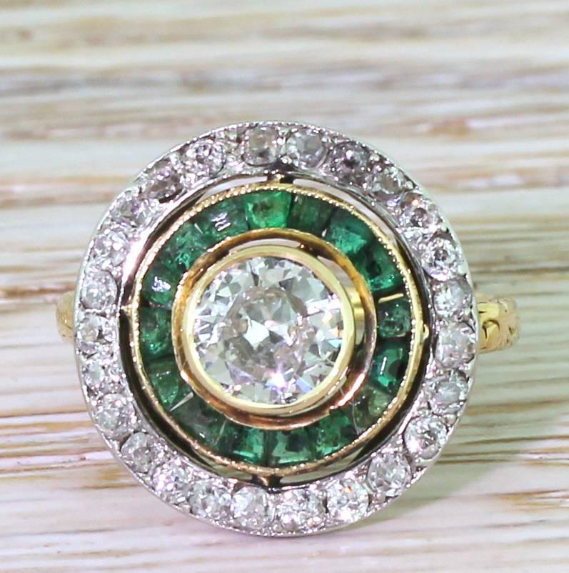 A wonderful find. The fabulously pretty target cluster ring features white and internally clean old European cut diamond of approximately 0.70 carat in the centre. Rubover set in yellow gold, the centre stone floats within a surround of calibré cut