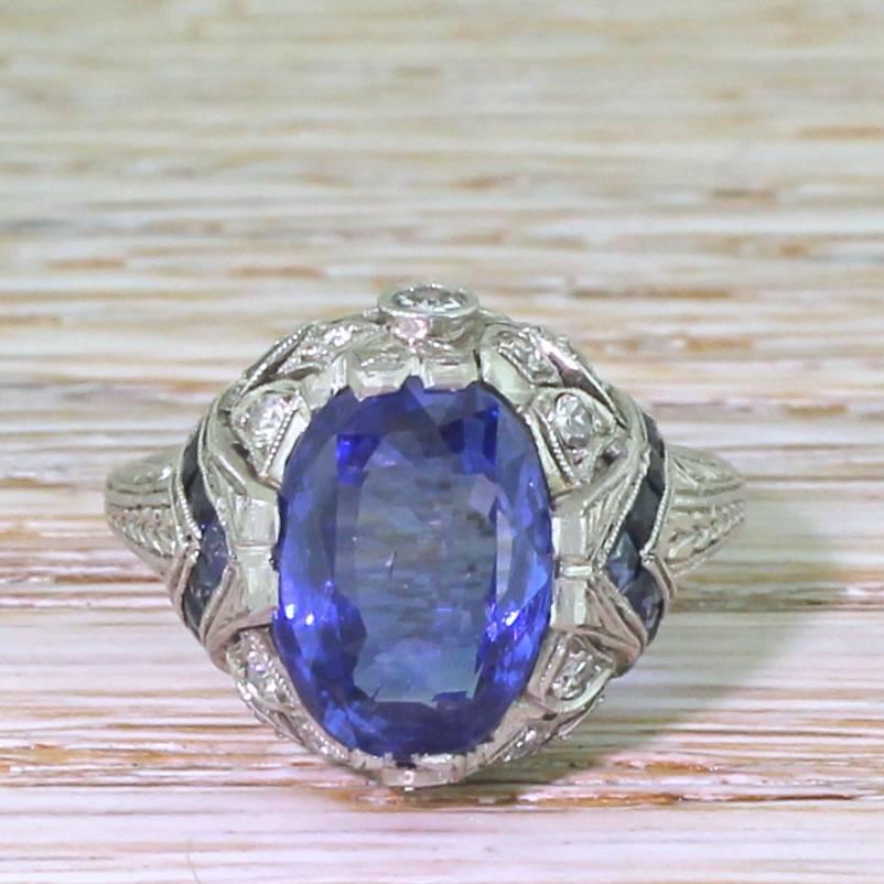 A top grade sapphire in an equally impressive mounting. The natural, no heat Ceylon sapphire in the centre displays the perfect cornflower blue; rich, bright, with clear flashes of violet and indigo. The stone in showcased in an exceptional highly