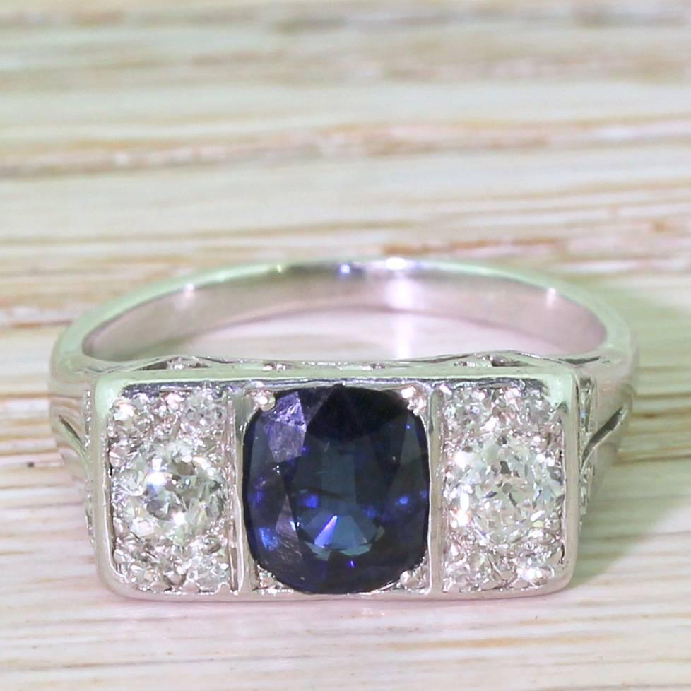 A stunner. The natural, unheated sapphire in the centre is box-set, and is flanked by a pair of diamond clusters. Each diamond box is centred by an old European cut with four eight-cut diamonds in the corners. The eye catching “V” gallery leads to