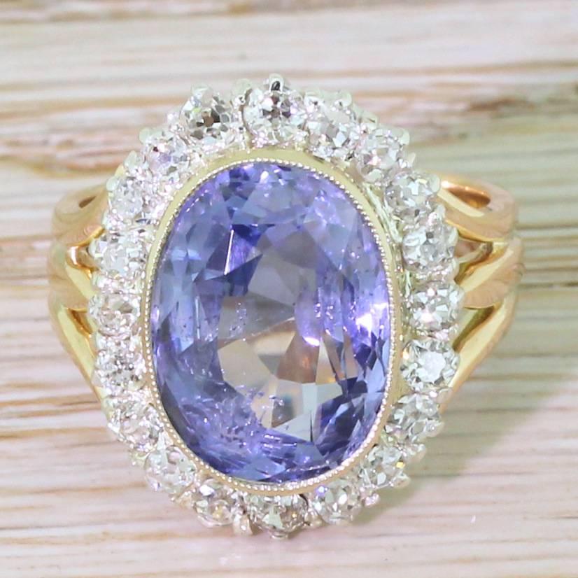 A glowing sapphire in a stunner of a ring. The natural and unheated Ceylon sapphire is a bright aqua blue and is veritably aglow with fire and brilliance. The centre is rubover and milgrain set within a surround of twenty old eight-cut diamonds in