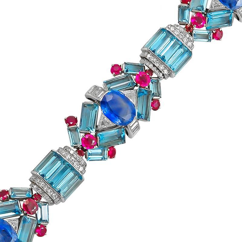 A fantastic 1930's art deco bracelet: designed as three main sections; each set with a central oval sapphire, within a baguette & trilliant-cut diamond surround, and geometrically spaced baguette aquamarines and circular rubies. 

The main