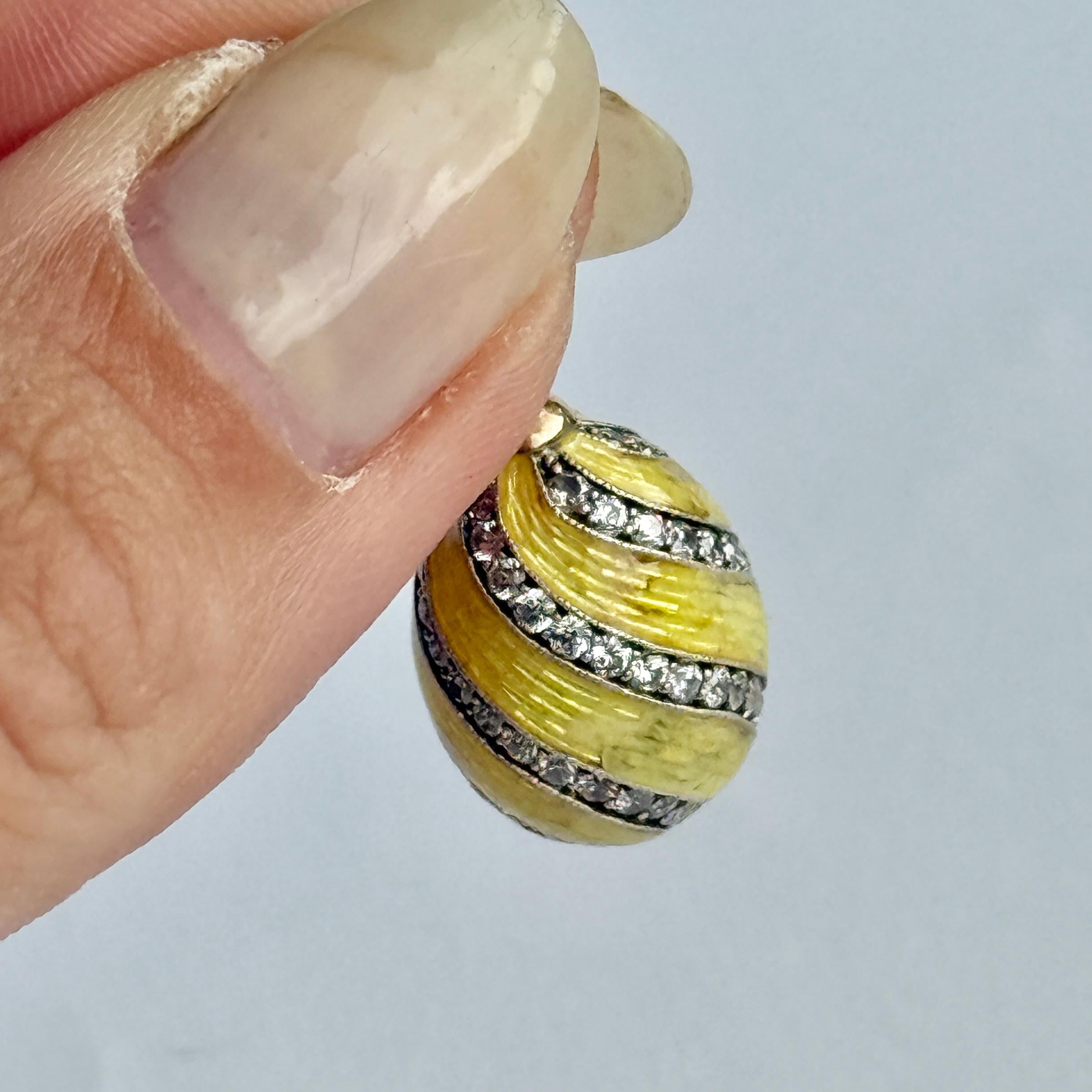 Questo splendido ciondolo è un uovo d'oro lucido a 14 carati rivestito di uno splendido smalto giallo. L'uovo d'oro è strutturato in modo da conferire allo smalto uno splendido effetto scintillante. Questo uovo contiene anche diamanti incastonati al