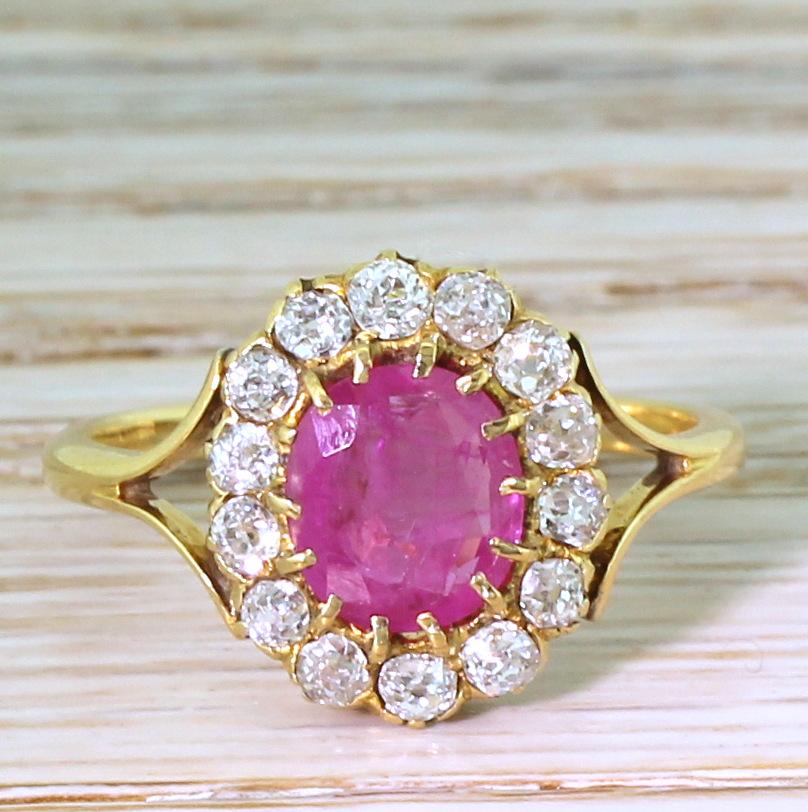 This antique ruby and diamond ring is, quite frankly, stunning. The bright, pinkish red ruby is claw set in yellow gold within a surround of fourteen high white, bright and clean old cut diamonds in a coronet setting. The head of the ring sits nice