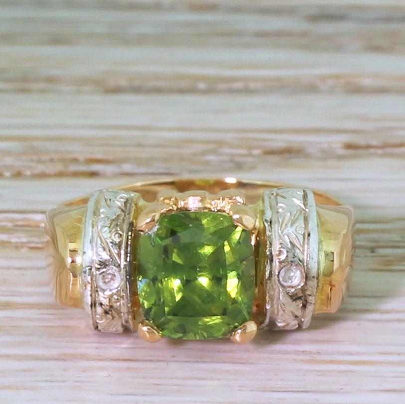 A marvellous ring. The demantoid garnet in the centre displays a hyper-charged bright electric green and is secured in a four claw open collet. The high shoulders feature two bands of finely engraved silver, each set with a small eight-cut diamonds,