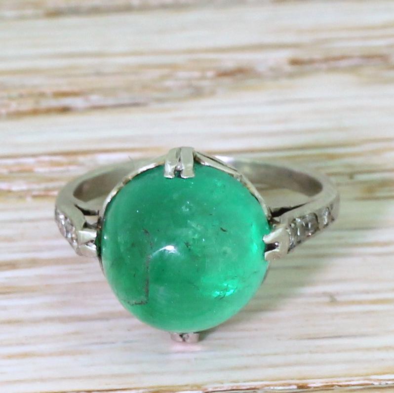 A heart-stoppingly beautiful Colombian cabochon emerald. The round, high-domed centre stone has an almost other worldly glow, and is certified as receiving only moderate oiling. The emerald is secured by four split claws with delightful skirt