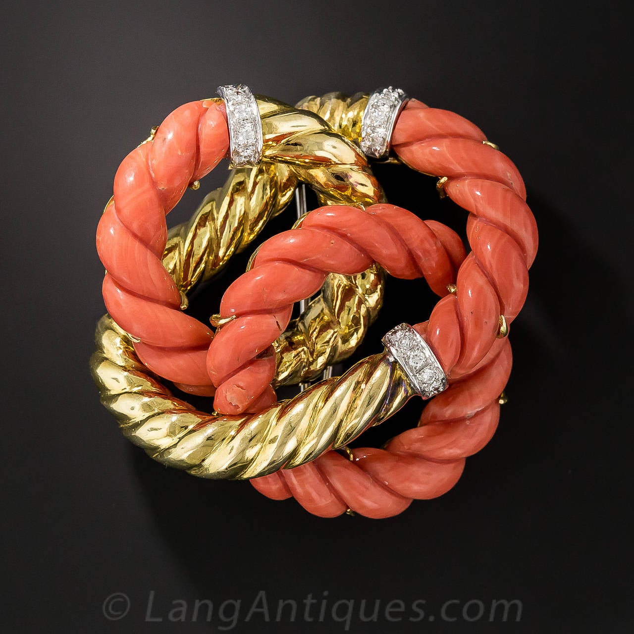 A trio of braided wreaths, composed of gleaming 18K yellow gold, natural orangey-salmon, handcarved coral and sparkling diamond bands, embrace to create this exceptional and very festive and wearable multidimensional sculpture. This ravishing and