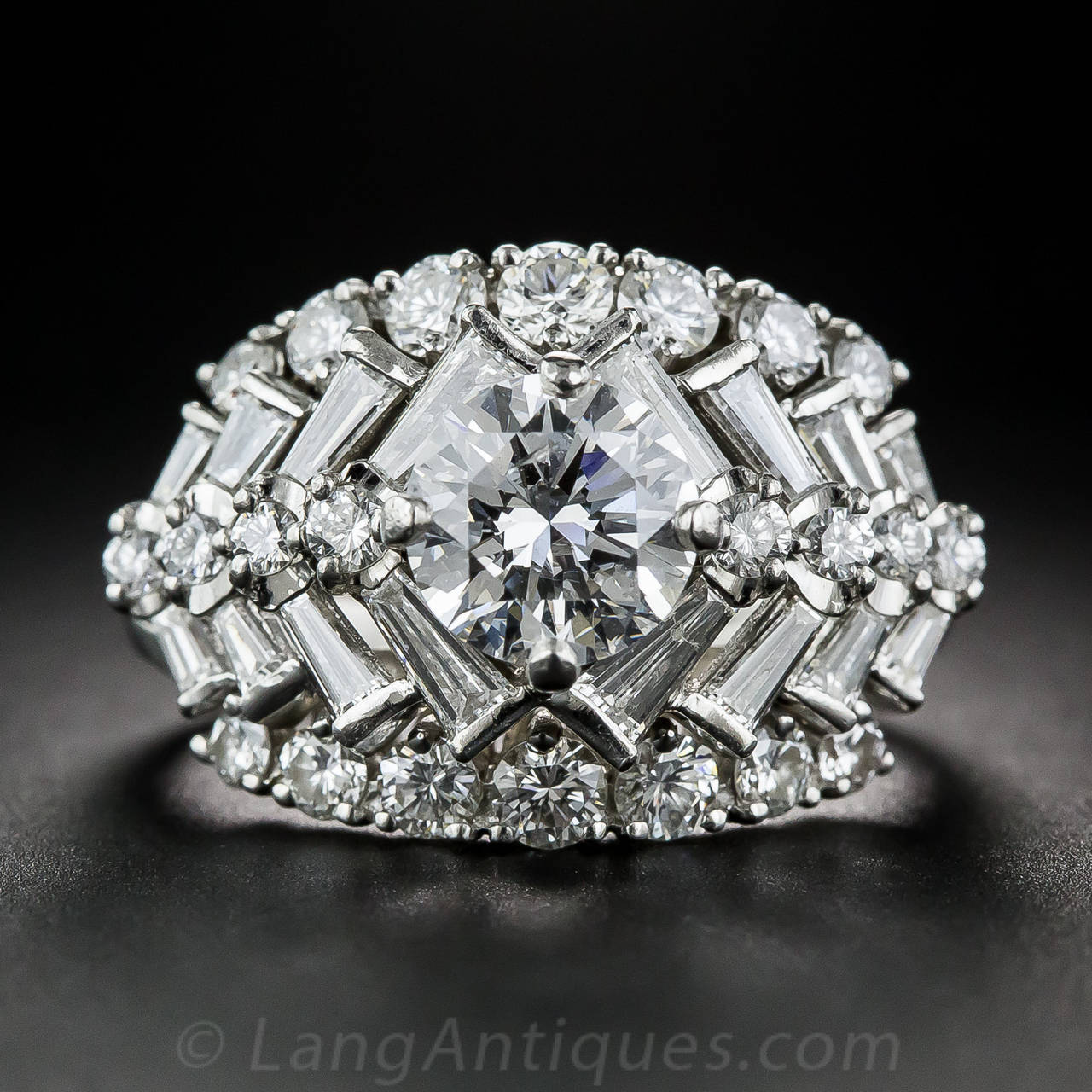 A bright, sparkling white, round brilliant-cut diamond, weighing 1.45 carats, is the crowning glory of this sensational, mid-twentieth century cocktail ring, artfully crafted in platinum. The elaborate geometric design is a highly stylized variation