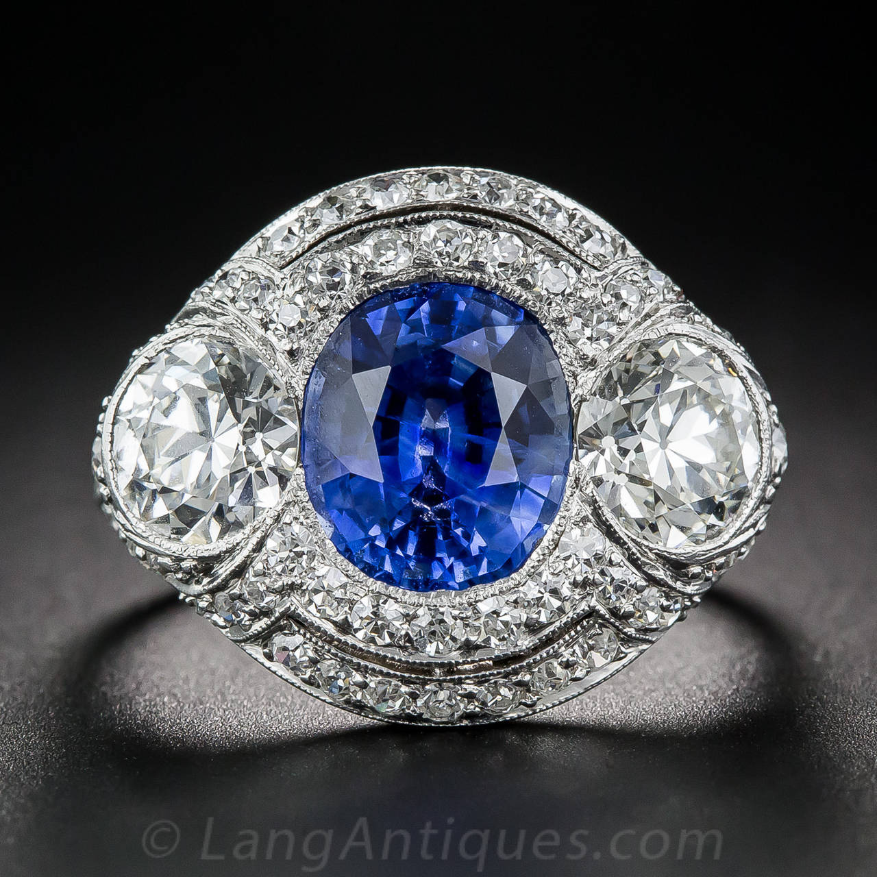 This magnificent Art Deco dazzler, circa 1920s-30s, features three gorgeous gemstones: a central 3.46 carat natural, electric cornflower blue sapphire, accompanied on each side by a pair of bright-white and sparkling European-cut diamonds weighing