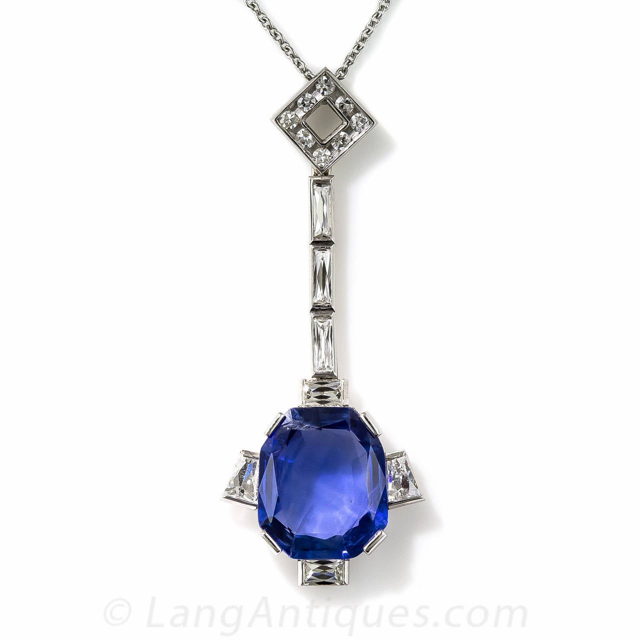 An enchanting royal blue, emerald-cut sapphire, weighing 5.50 carats, unusually fashioned with slightly flared sides, is majestically presented in this sleek and sexy Art Deco inspired platinum and diamond lavaliere necklace. The natural colored,