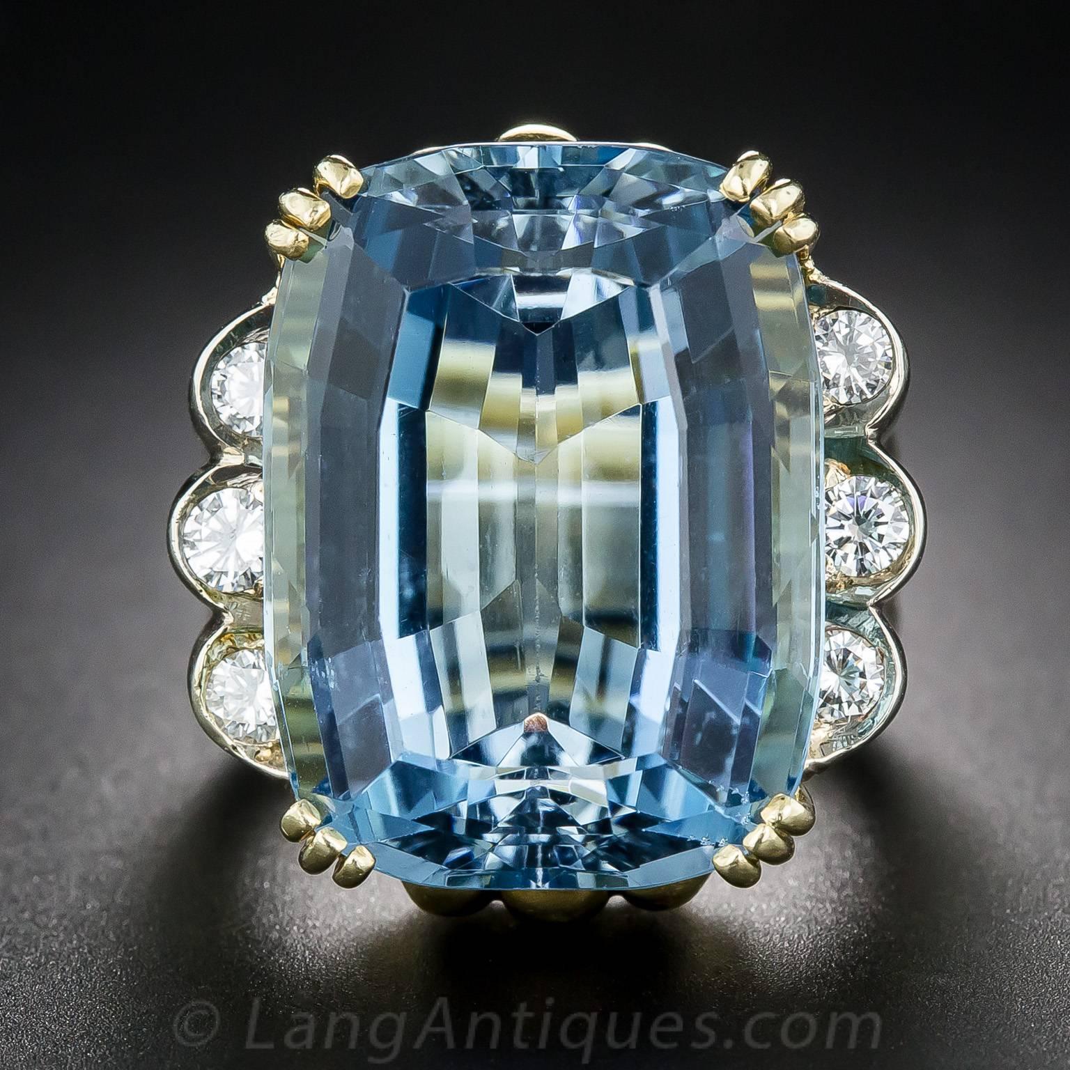 A gorgeous, deeply saturated, faceted cushion shape aquamarine, weighing in at an impressive 27 carats, radiates a magnificent Mediterranean-blue hue. The gemmy gemstone is stylishly presented in a comfortable 18 yellow gold mounting designed with a