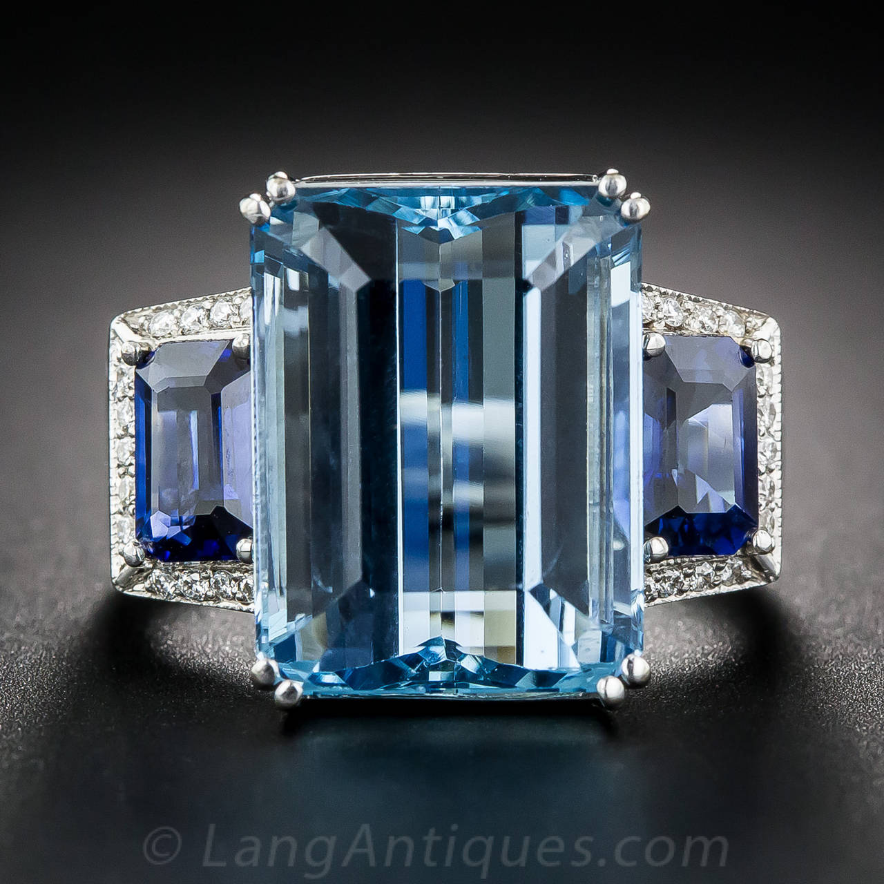 A gem Santa Maria aquamarine, weighing 11 carats, displaying about the finest, deeply saturated color imaginable, glistens and glows between a matched pair of rich, royal blue, emerald-cut sapphires, weighing over one carat each, framed on three