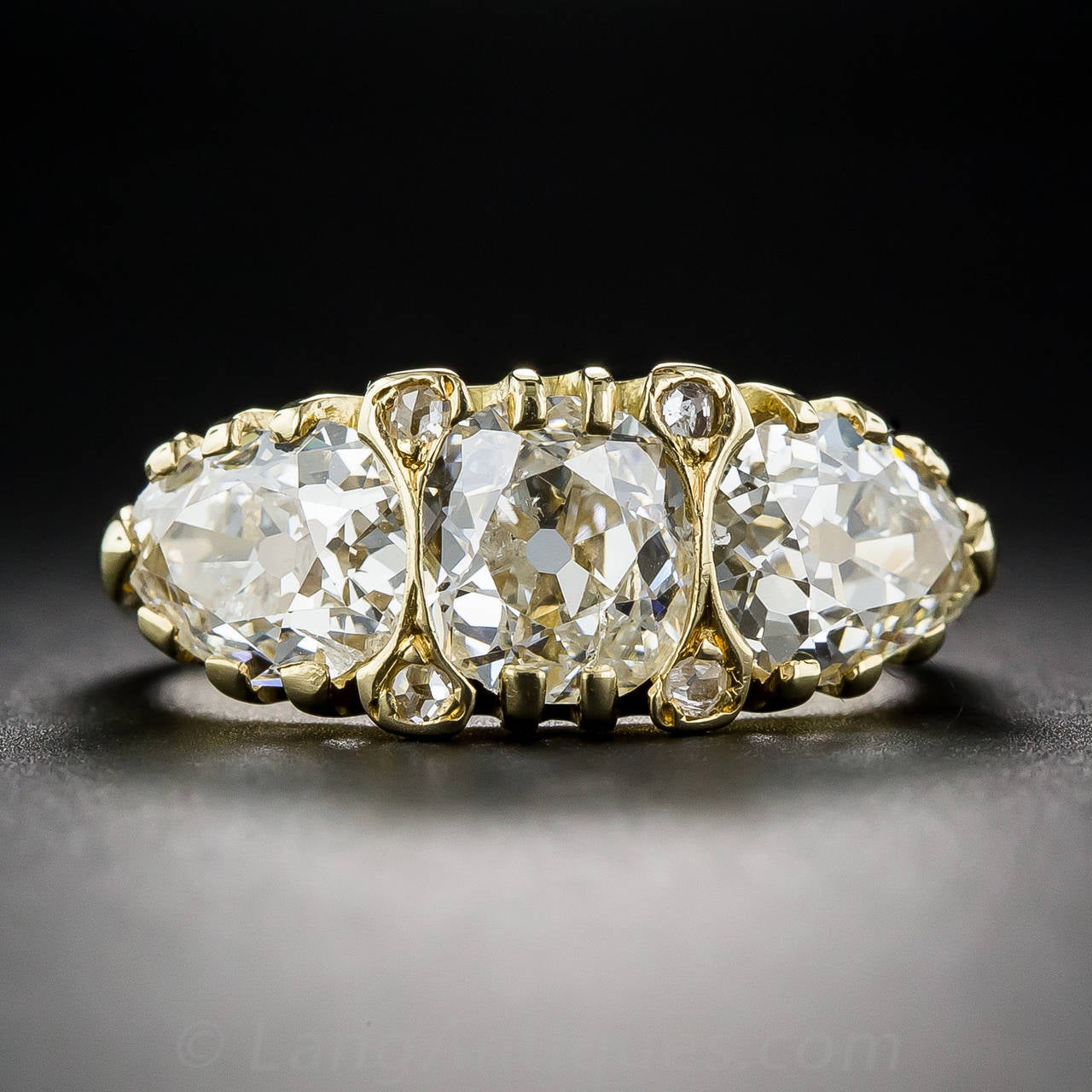 A dazzling trio of early-20th century diamonds: a 1.00 carat antique cushion in the center, and on the sides, two old mine pear shapes together weighing 1.60 (but they present all of 1 carat each), sparkle in all directions in this classic 18K