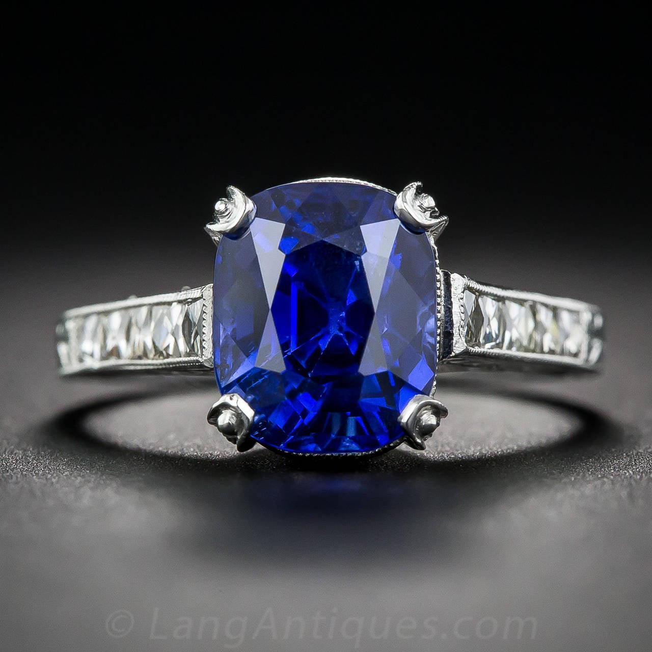 A seriously 'gemmy', natural, no-heat sapphire, weighing 4.90 carat and originating from old Burma beams from within a newly handmade platinum mounting, rendered in enduring vintage style, enlivened with French-cut diamonds shimmering along the
