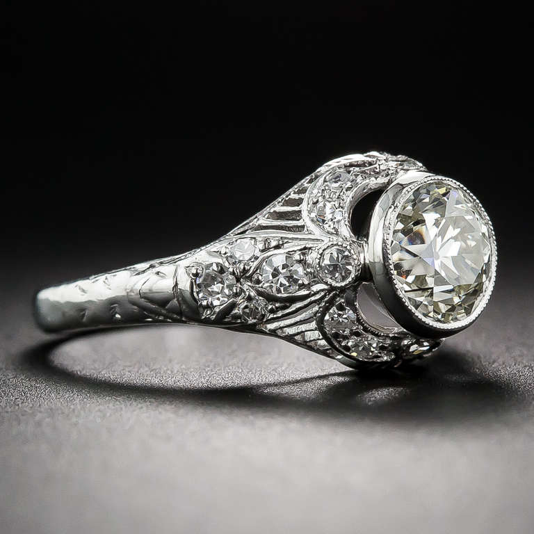 A sparkling collet-set European-cut diamond, weighing 1.10 carats, is held aloft by a glittering garland motif in this elegantly detailed, 1920s vintage, diamond engagement ring, hand-fabricated in platinum with delicate diamond-set neoclassical