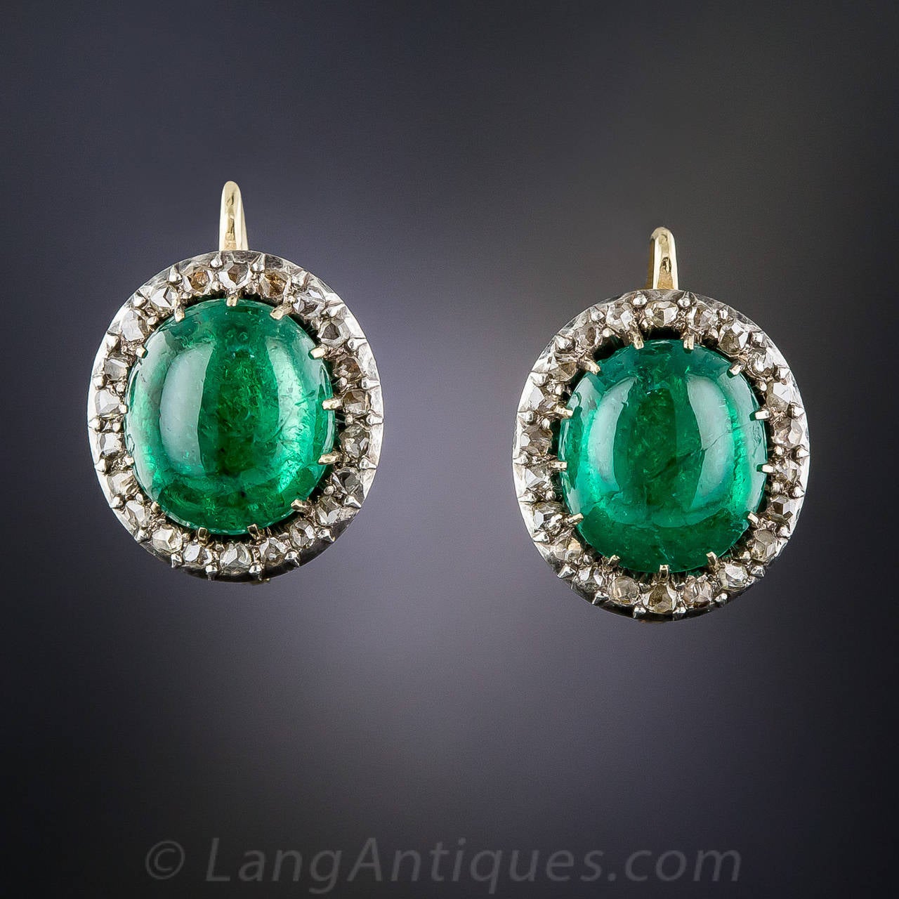 A gorgeous, delectable pair of deeply saturated, rich green gumdrops (aka cabochon emeralds), with a total weight of 8.00 carats, are traditionally presented in glittering rose-cut diamond halos, expertly hand fabricated in silver over gold - circa