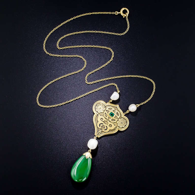 This enchanting, exotic and far-from-ordinary turn-of-the-twentieth century jewel highlights a translucent green natural Burmese jade drop that swings freely from a magnificently ornamented golden escutcheon centered with an all-seeing emerald eye.