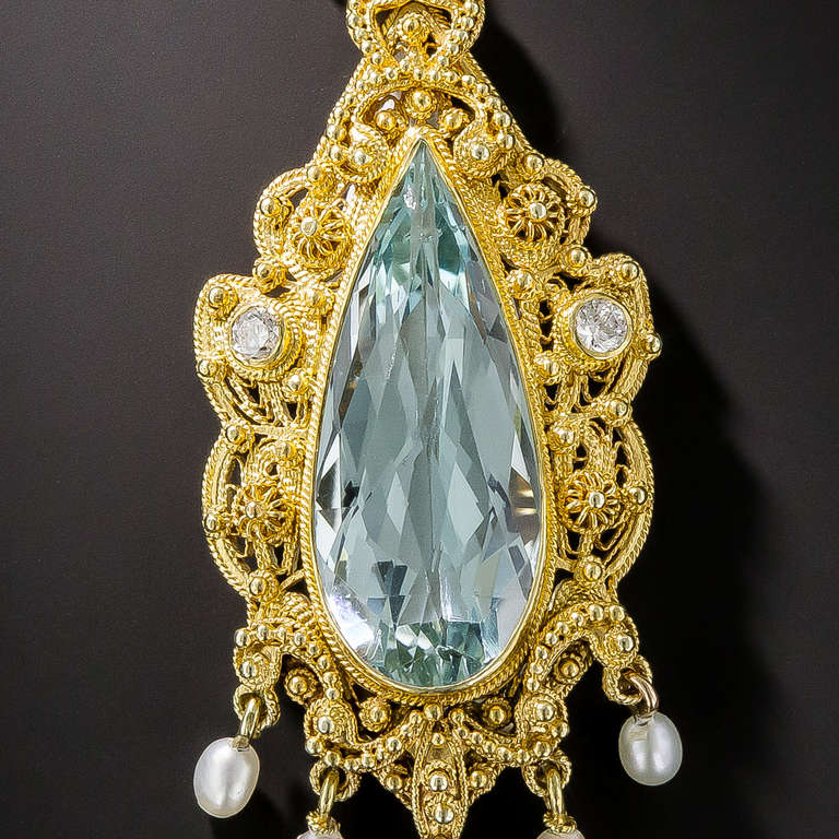 A slender, elegantly proportioned pear shape aquamarine, with a rose-cut faceted top and displaying a bright, icy-blue hue, is fancifully presented in a rich golden filigree and cannetille frame dotted with a trio of diamonds (one on the matching