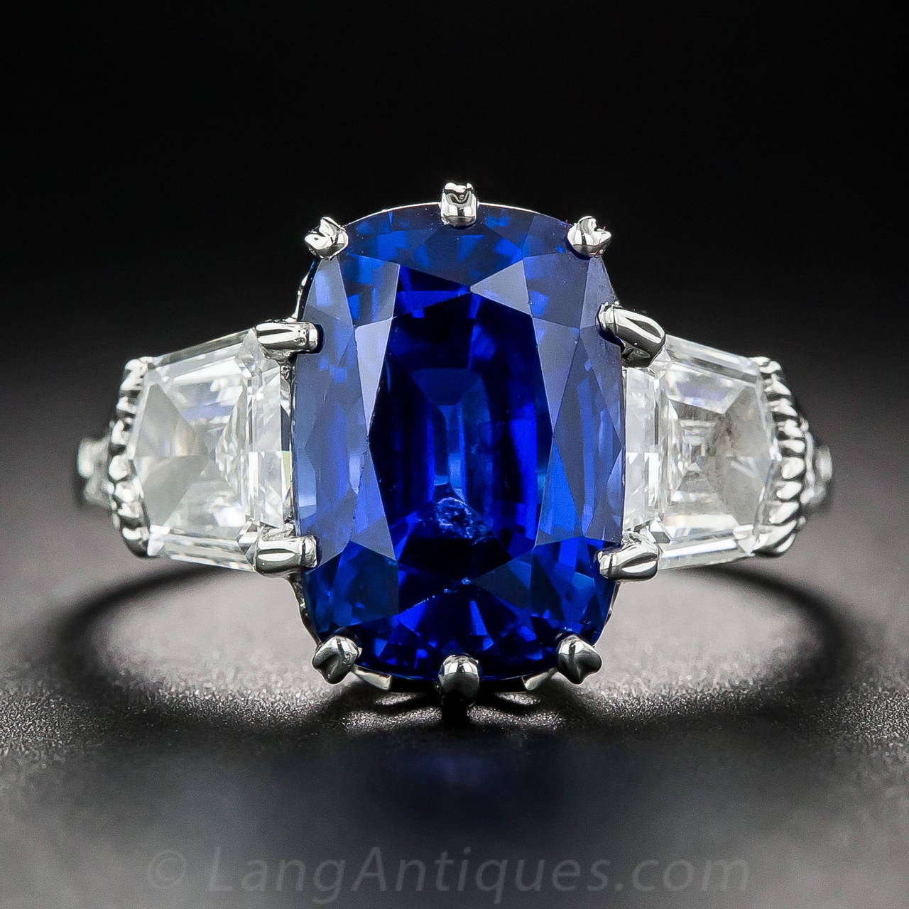 Natural sapphires this big, beautiful and radiant blue are a rare find, and this 7.18 carat stunner is naturally impressive and breathtaking with no heat treatment. Two crisp epaulette-cut white diamonds, together totaling just over one carat,