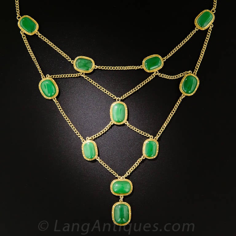 A collection of fourteen matched, natural, deep apple green jade cabochons, each framed in a hand engraved 18K gold bezel, are artfully arrayed in this rare and wonderful swag necklace hailing from 1930s-40s China or Hong Kong; however, the jades