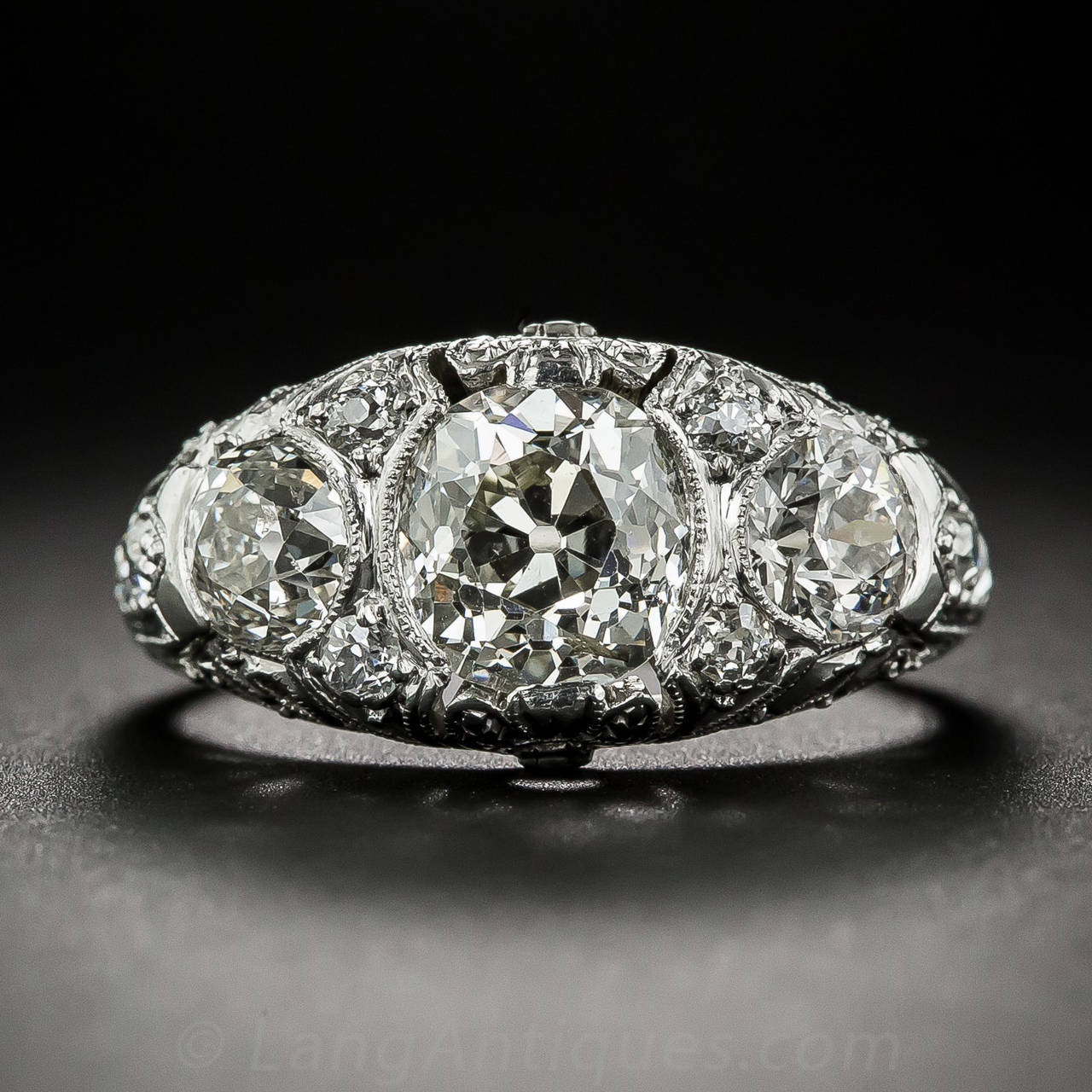 An exemplary original early-Art Deco (circa 1920) three-stone ring, elegantly handcrafted in platinum and featuring, in the center, a sparkling old mine-cut diamond weighing one-and-a-half carats. The sun-bright diamond is aided and abetted, left