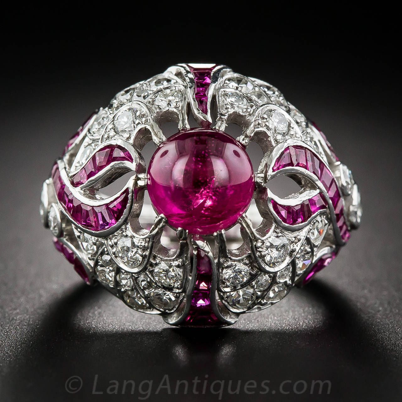 Here is an original  Art Deco showstopper from the 1920s - 1930s. This sizzling and sizable bombe domed ring centers on a bright and lively round cabochon ruby weighing 4.05 carats. Bright-red flames of calibre-cut rubies sweep up the sides against