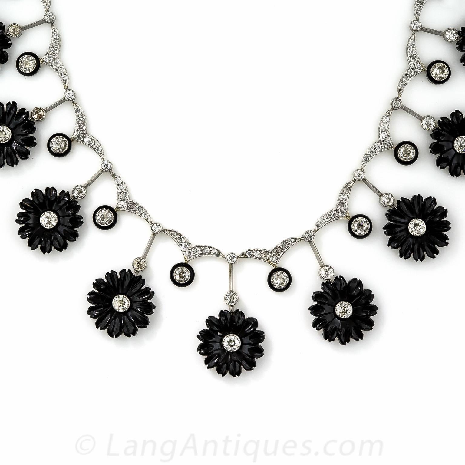 A unique and supremely beautiful late-Edwardian/early-Art Deco necklace in glorious black & white. 15 hand carved, diamond centered onyx flowers alternate with black enamel outlined European-cut diamonds, all of which suspend from a glittering