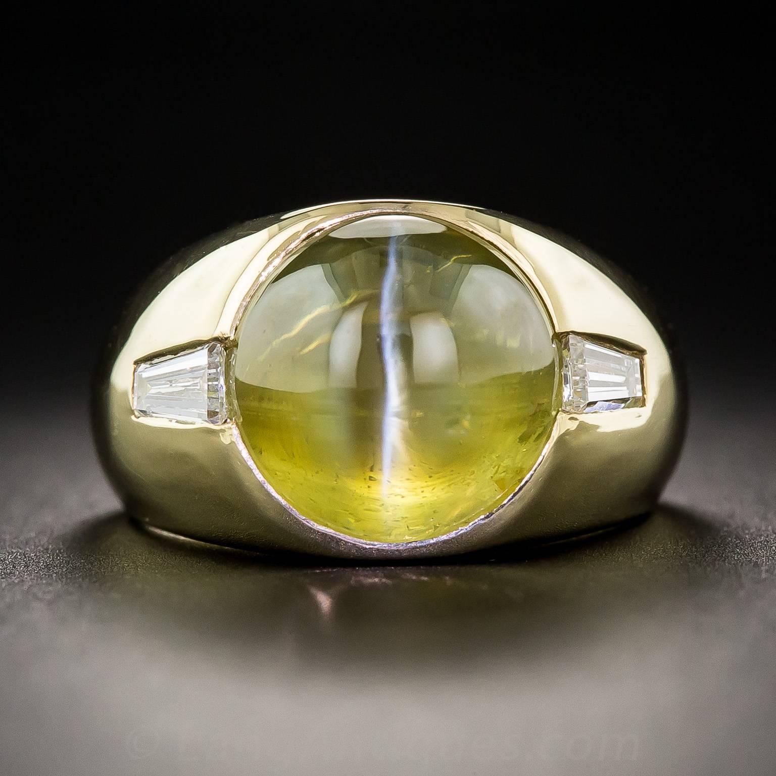 Imbued with a glowing, crystalline, honey-colored hue (with just a touch of khaki green), this perfectly proportioned chrysoberyl cat's-eye, weighing 10 carats, winks its straight white eye from between a pair of bright white tapered baguette