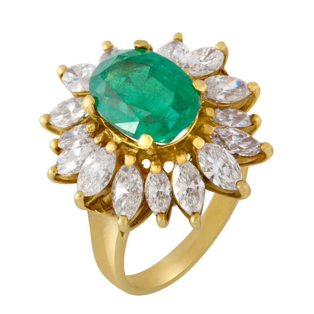 This ring features an oval cut emerald ring that prong set into an 18k yellow gold setting. Surrounding the center stone are sixteen (16) white marquise diamonds that point outwards in a sunburst fashion. Each diamond is individually prong set as