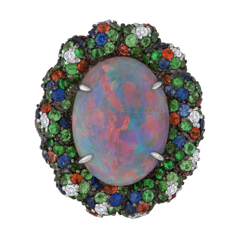 This design features an Australian black opal that presents us with a play of color that ranges from green and blue to pink and red. The center stone is prong-set in an 18k white gold setting that is studded with a variety of precious gemstones that