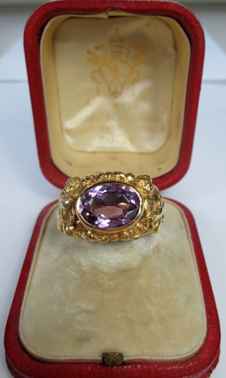 This ring is designed out of with an oval faceted collet set amethyst.
The 18Kt chased setting decorated with puttis holding religious symbols cups and tiara

The ring has been made during the Pope Leone XIII (Gioacchino Pecci) 1878-1903 reign.