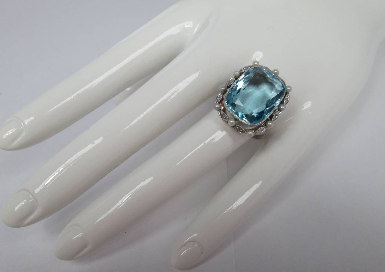 The millegrain set cushion cut aquamarine weighing approx. 12 cts to a border designed as a 
wreath
set with pearls and rose cut diamonds
Mounted in 18Kt white gold

Finger size: 7

Weight: 7.6 gr