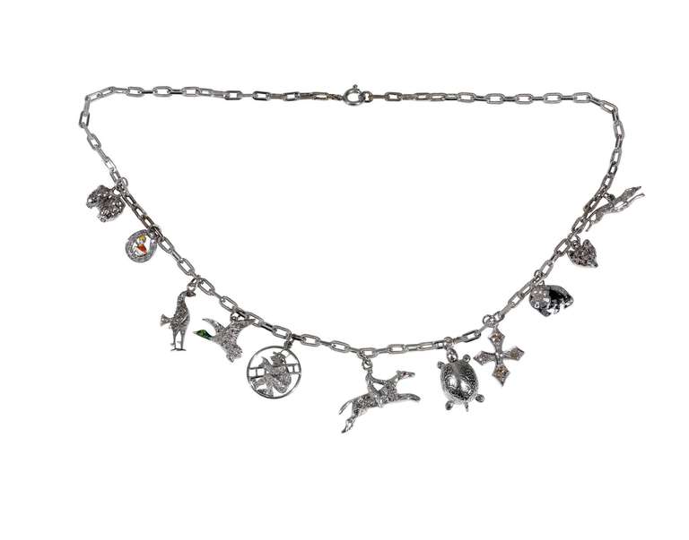 A multi gem-set charm necklace, the fetter link 18kt white gold chain, supporting eleven charms, each depicting a different subject, including a fox, dog,tortoise,cross,horse,phaesant,bird,jockei and
variously decorated with small single-cut and