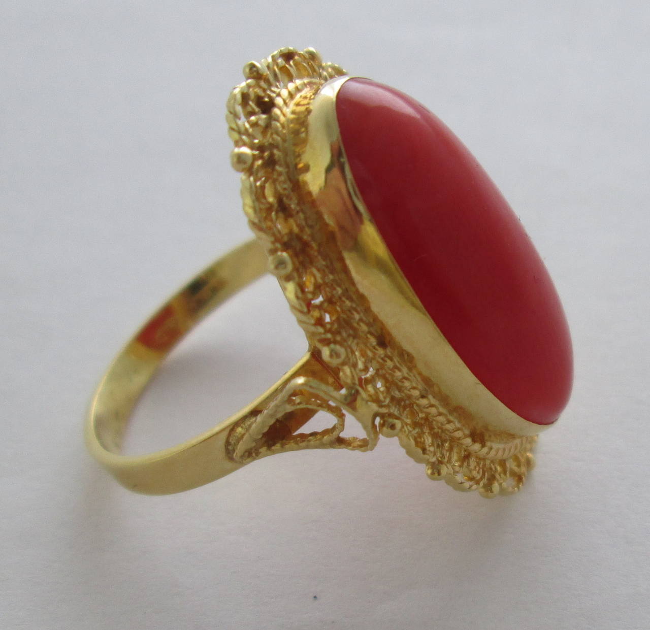The collet set large smooth cabochon coral, approx 21 x 10 mm within an ornate filigree frame.

Mounted in 18Kt yellow gold

Finger size: 6 1/2

Weight: 6.2 gr