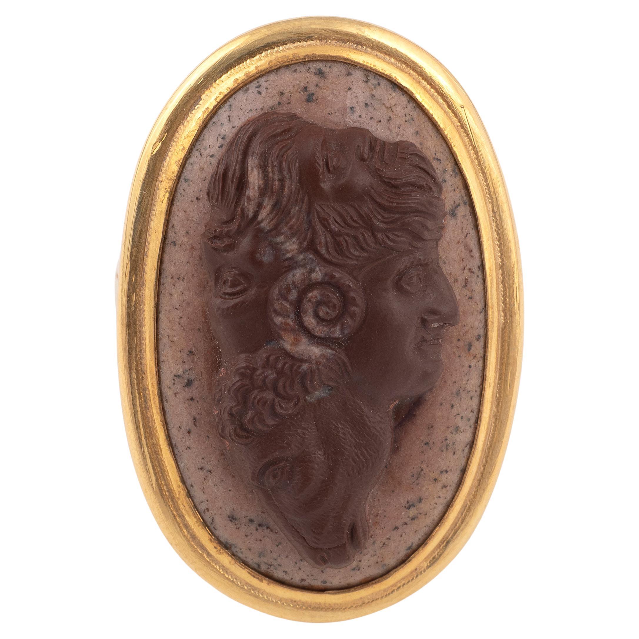
Oval, depicting four conjoined heads: a male youth, a ram, a satyr and a bearded man, within a gold mount, ring size 7 length 23mm, width 14mm
A gryllus is a group of conjoined heads, usually fanciful combinations of beasts and humans, often with