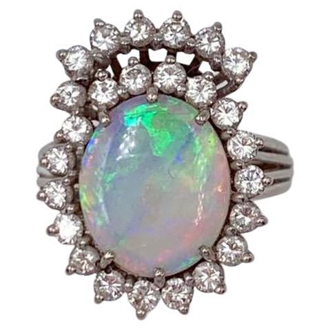 
Stilisierter Ring aus durchbrochenem Weißgold 750, in dessen Zentrum ein ovaler Opal steht, der von Diamanten im Brillantschliff umgeben und unterstrichen wird. Circa 1970.
Finger: 53. Bruttogewicht: 5 g. 
