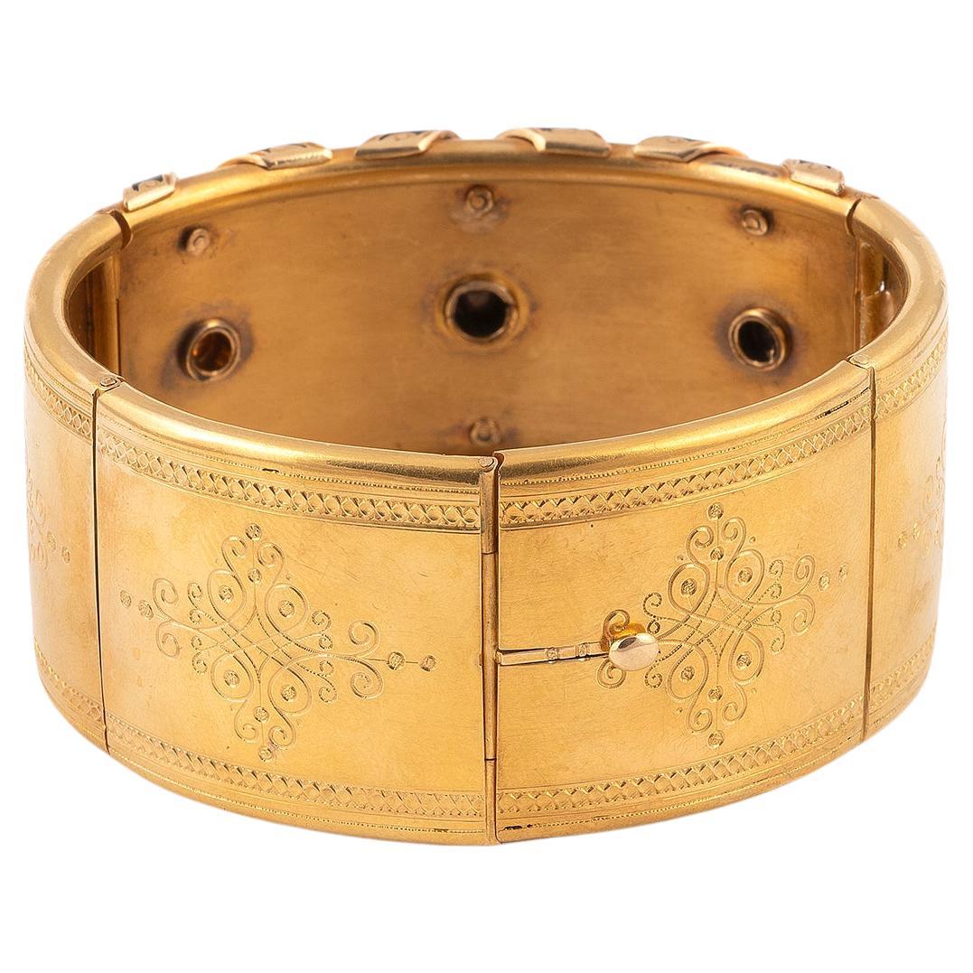 

Semi-rigid and articulated bangle bracelet in 18kt yellow gold engraved with foliage decoration, the central motif black enamel  decorated with braces formed by natural pearls and rose cut diamonds on a silver setting.  French work from the 19th