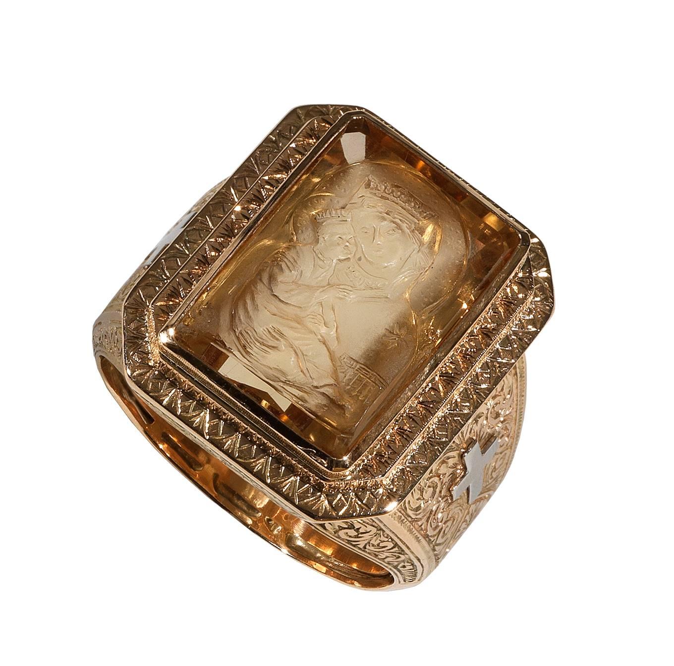 The large rectangular shape step cut citrine with intaglio carved depicting the Madonna and Child, collet set within a heavy 18Kt rose and yellow gold mounted, scroll engraved throughout, a cross in white gold on both shoulders.

Size of the