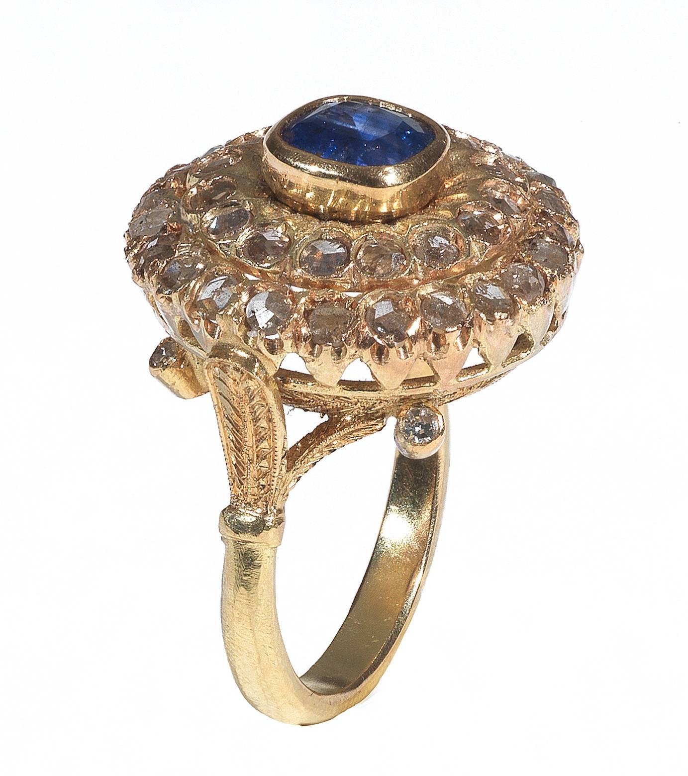 The central cushion-cut sapphire to a rose-cut diamond cluster surround, the carved and engraved gallery to a foliate trifucarted shoulders and plain hoop. Mounted in yellow gold.

Weight: 8.8 gr
Finger size: 7